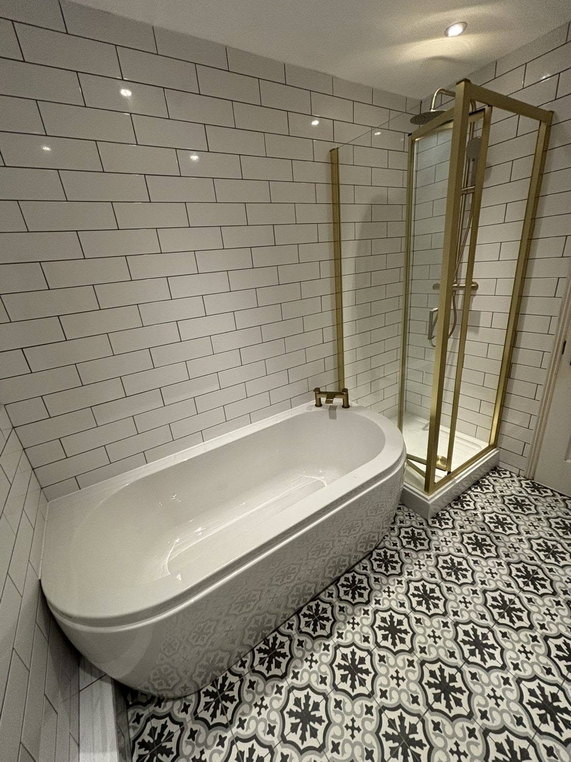 Gold-framed shower enclosure with patterned floor tiles and bath